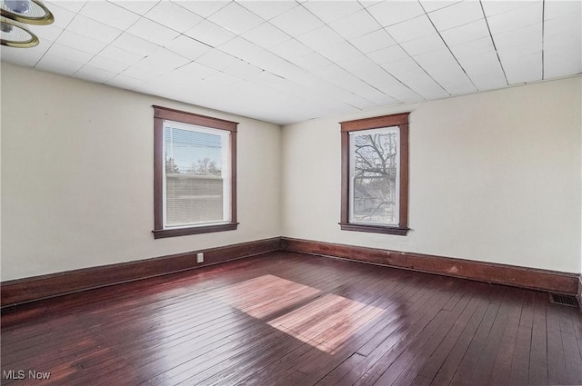 empty room with dark wood-type flooring, visible vents, and baseboards