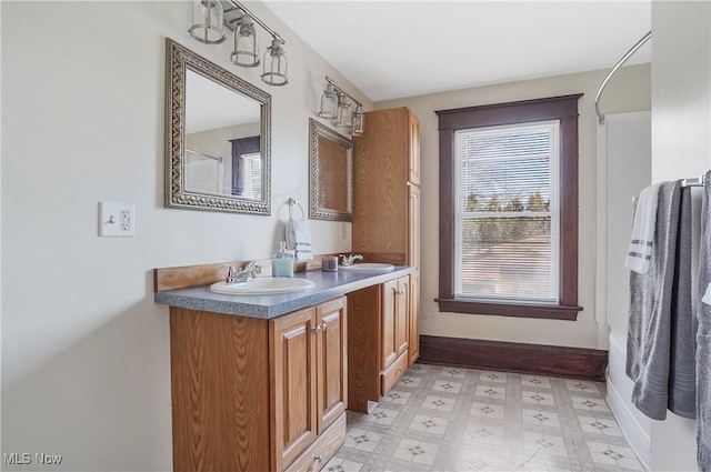 bathroom with baseboards, double vanity, a sink, and tile patterned floors