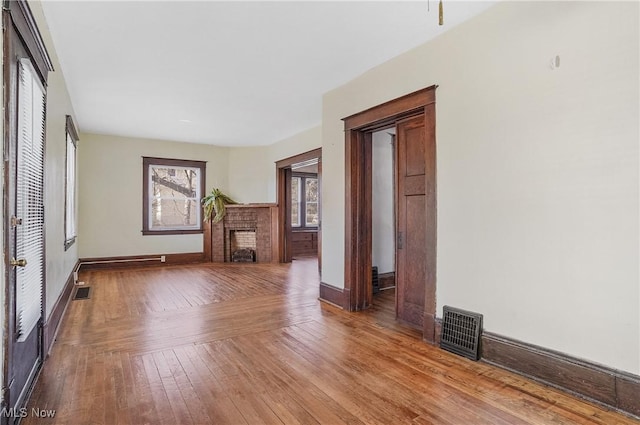 unfurnished living room with hardwood / wood-style flooring, a brick fireplace, visible vents, and baseboards