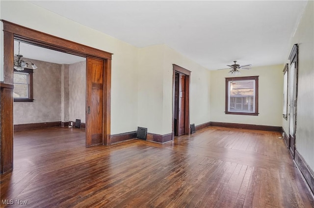 spare room featuring ceiling fan with notable chandelier, wood-type flooring, and baseboards