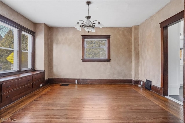 unfurnished dining area featuring a chandelier, wood-type flooring, visible vents, and baseboards