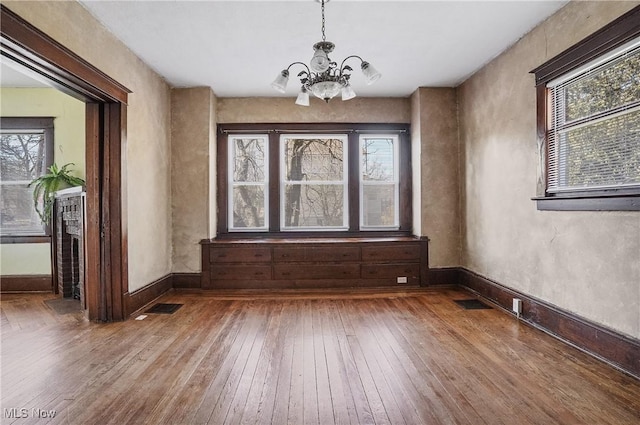 unfurnished dining area featuring baseboards, visible vents, hardwood / wood-style floors, and an inviting chandelier