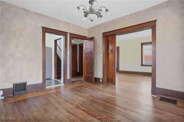 empty room with hardwood / wood-style floors, stairway, visible vents, and a notable chandelier