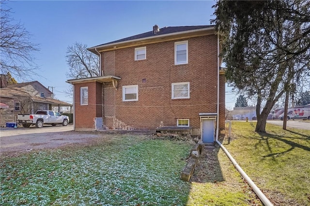 back of house with a yard, brick siding, and a chimney