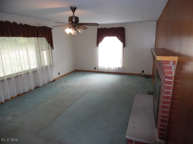 unfurnished living room featuring carpet, a brick fireplace, ceiling fan, and baseboards