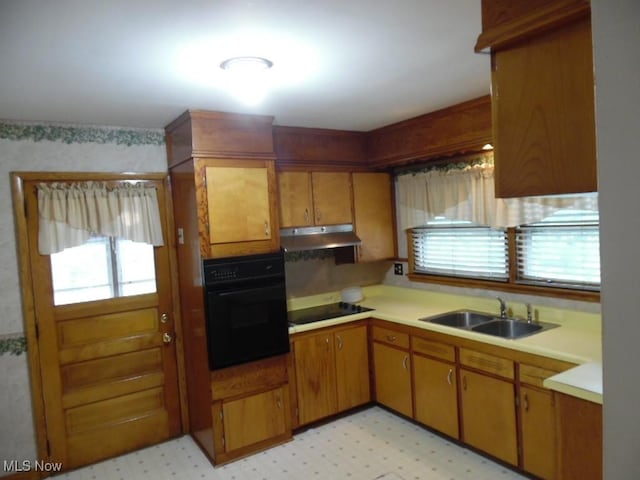 kitchen featuring light floors, under cabinet range hood, light countertops, black appliances, and a sink