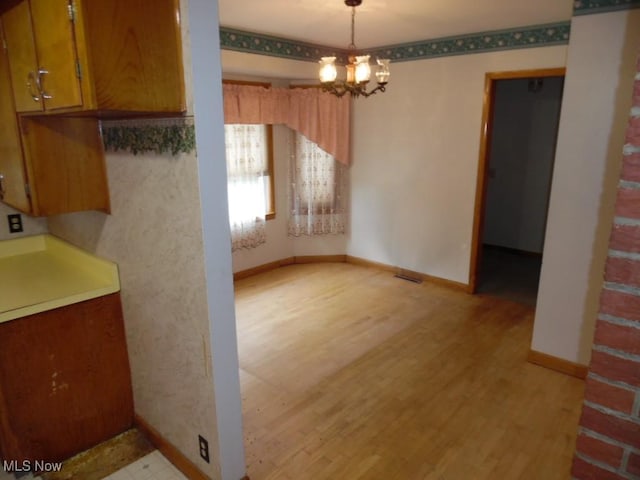 unfurnished dining area featuring light wood-type flooring, baseboards, and an inviting chandelier