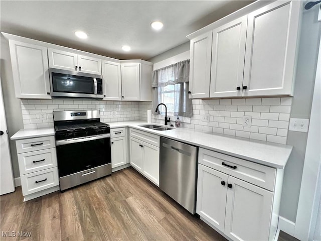 kitchen featuring stainless steel appliances, a sink, white cabinets, light countertops, and dark wood finished floors