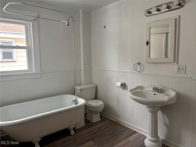 bathroom with a soaking tub, toilet, wainscoting, wood finished floors, and walk in shower