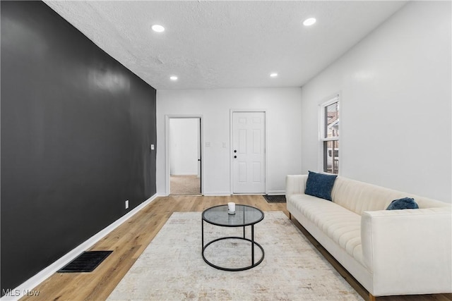 living room with light wood-type flooring, visible vents, baseboards, and recessed lighting