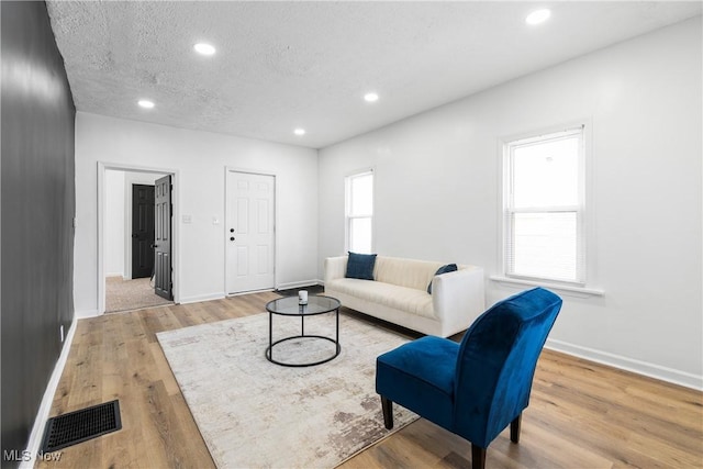 living room with light wood-type flooring, visible vents, a textured ceiling, and recessed lighting