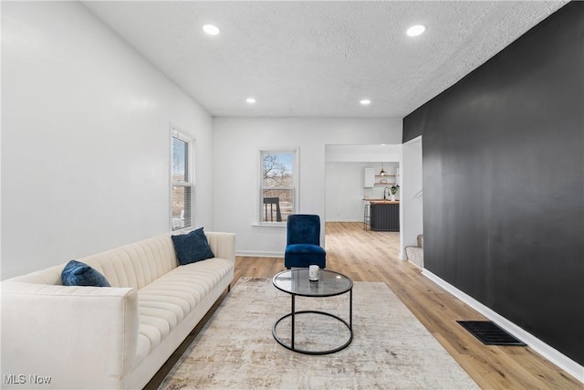 living area with light wood finished floors, baseboards, visible vents, and a textured ceiling