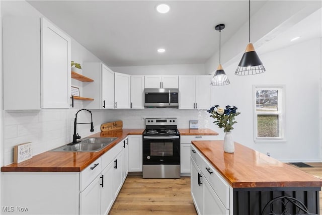 kitchen featuring open shelves, stainless steel appliances, white cabinets, a sink, and wood counters