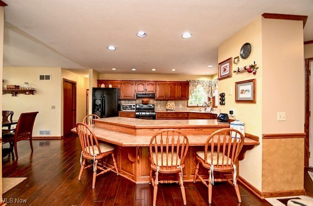 10400 Stoneacre St NW, Canal Fulton, OH 44614 - kitchen with black fridge with ice dispenser, gas stove, a peninsula, dark wood-style flooring, and a breakfast bar