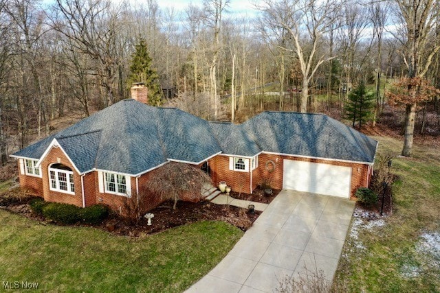 single story home featuring a garage, brick siding, concrete driveway, a chimney, and a front yard