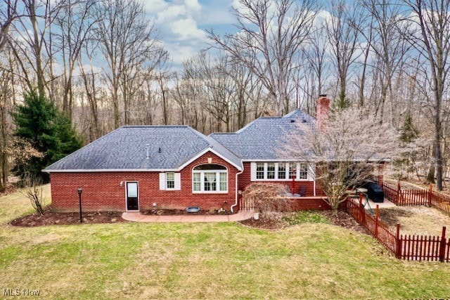 rear view of house featuring brick siding, a chimney, fence, and a yard