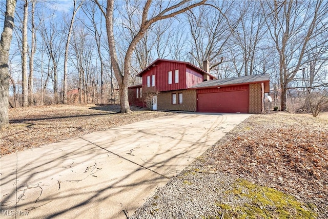 view of property exterior with concrete driveway, brick siding, a chimney, and an attached garage