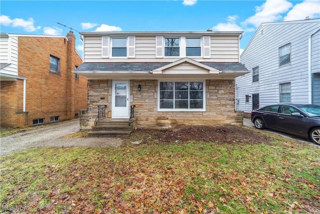 view of front of property featuring entry steps, stone siding, a shingled roof, and a front yard