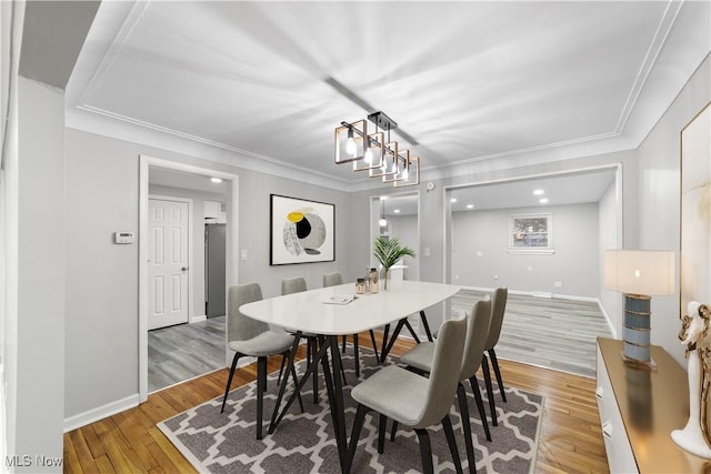 dining room with baseboards, hardwood / wood-style floors, an inviting chandelier, and crown molding