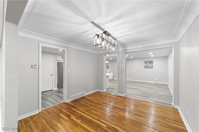 unfurnished room with ornamental molding, wood-type flooring, visible vents, and baseboards