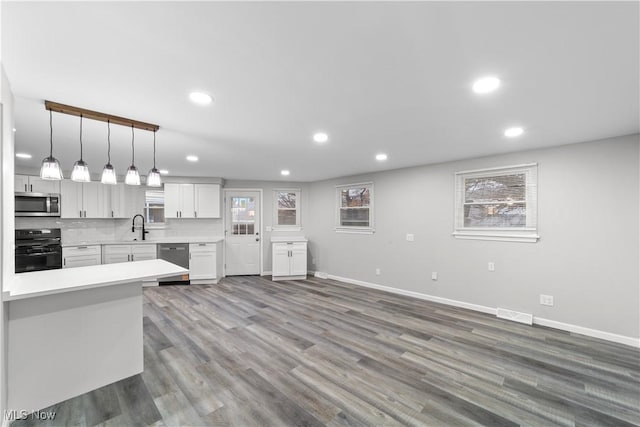 kitchen with light countertops, appliances with stainless steel finishes, white cabinets, a sink, and wood finished floors