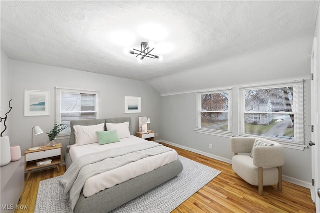 bedroom featuring a textured ceiling, baseboards, vaulted ceiling, light wood-type flooring, and an inviting chandelier