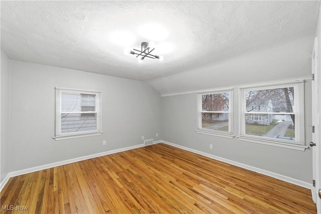 empty room featuring visible vents, vaulted ceiling, a textured ceiling, wood finished floors, and baseboards