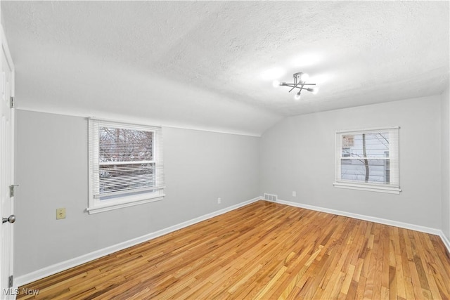 additional living space featuring visible vents, baseboards, vaulted ceiling, a textured ceiling, and light wood-style floors