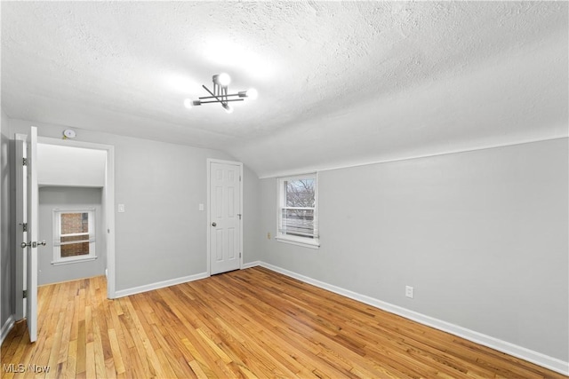 unfurnished bedroom with light wood-type flooring, baseboards, vaulted ceiling, and a textured ceiling