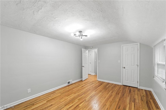 unfurnished bedroom featuring lofted ceiling, visible vents, light wood-style floors, a textured ceiling, and baseboards