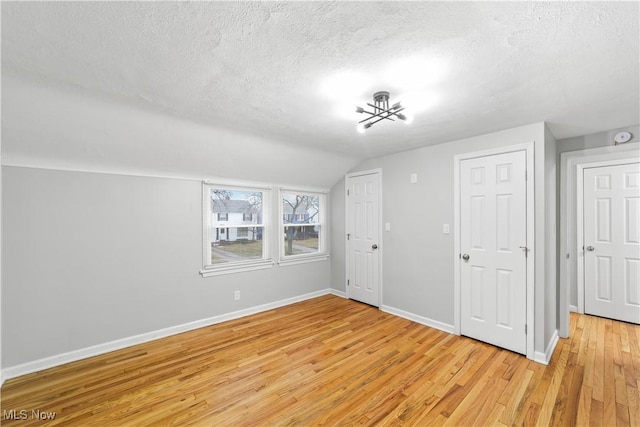 additional living space with a textured ceiling, lofted ceiling, light wood-style flooring, and baseboards