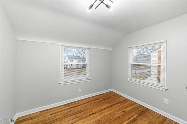 empty room featuring baseboards, vaulted ceiling, and wood finished floors