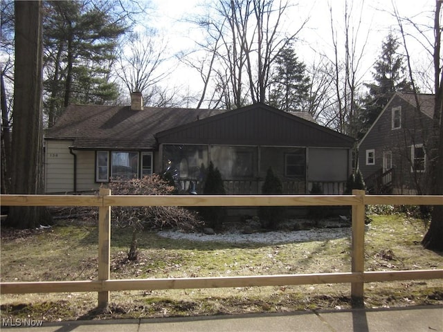 view of front of home featuring a sunroom, a chimney, fence, and roof with shingles