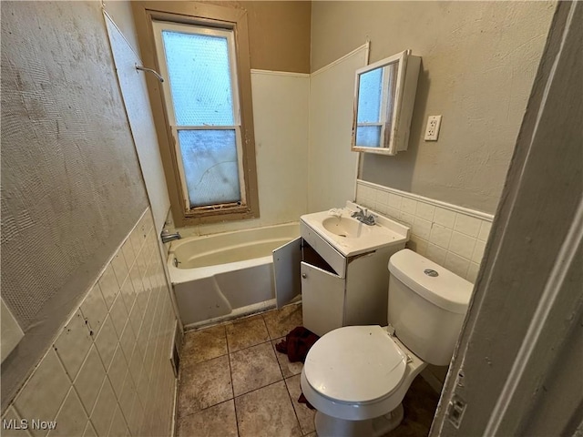 bathroom with tile walls, toilet, a bathing tub, vanity, and tile patterned floors