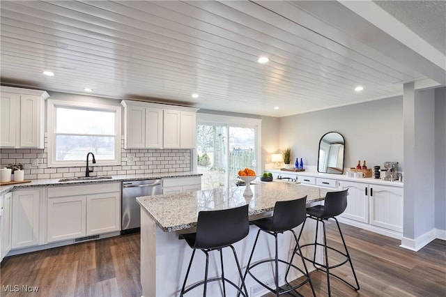 kitchen with dark wood-style flooring, a sink, stainless steel dishwasher, tasteful backsplash, and a kitchen bar