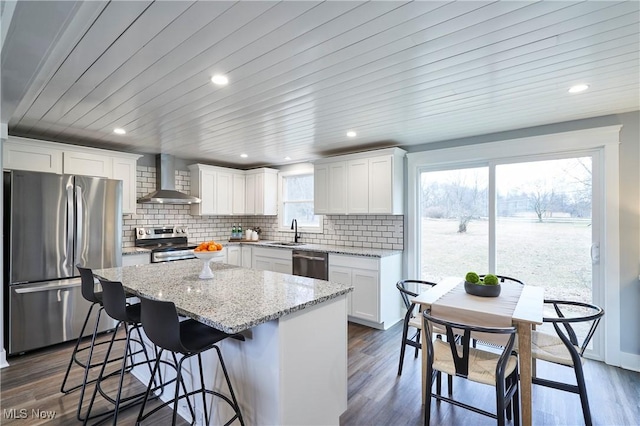 kitchen featuring dark wood-style floors, a center island, tasteful backsplash, appliances with stainless steel finishes, and wall chimney range hood