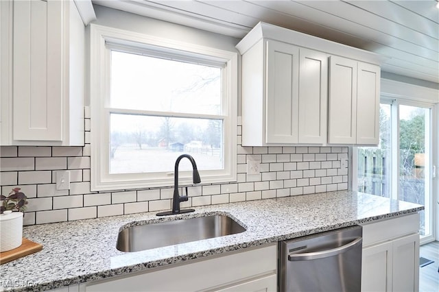 kitchen with tasteful backsplash, white cabinets, dishwasher, and a sink