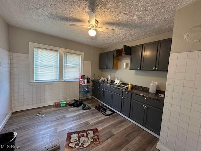 kitchen featuring ceiling fan, a textured ceiling, dark wood-type flooring, tile walls, and dark countertops