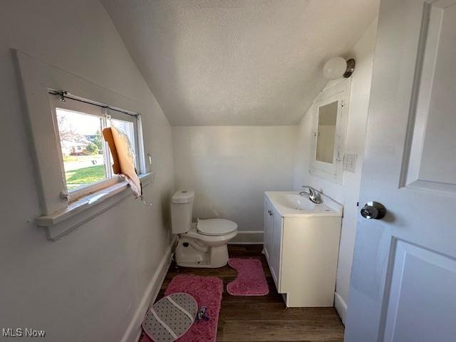 bathroom featuring toilet, vaulted ceiling, a textured ceiling, wood finished floors, and baseboards