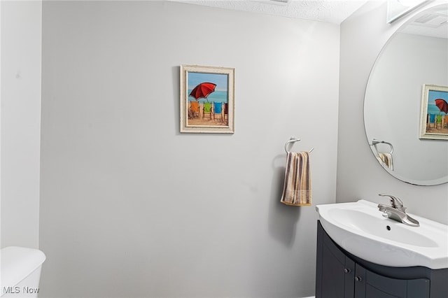 half bath with toilet, visible vents, a textured ceiling, and vanity