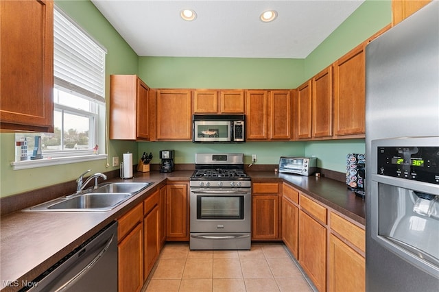 kitchen featuring stainless steel appliances, dark countertops, a sink, and light tile patterned floors