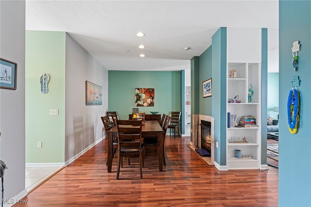 dining room with baseboards, built in features, wood finished floors, and a glass covered fireplace