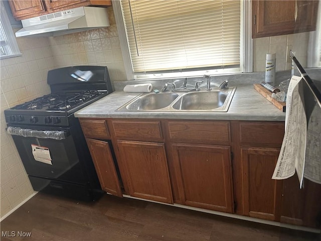 kitchen featuring under cabinet range hood, a sink, light countertops, brown cabinets, and gas stove