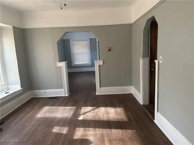 spare room with arched walkways, visible vents, baseboards, and wood finished floors