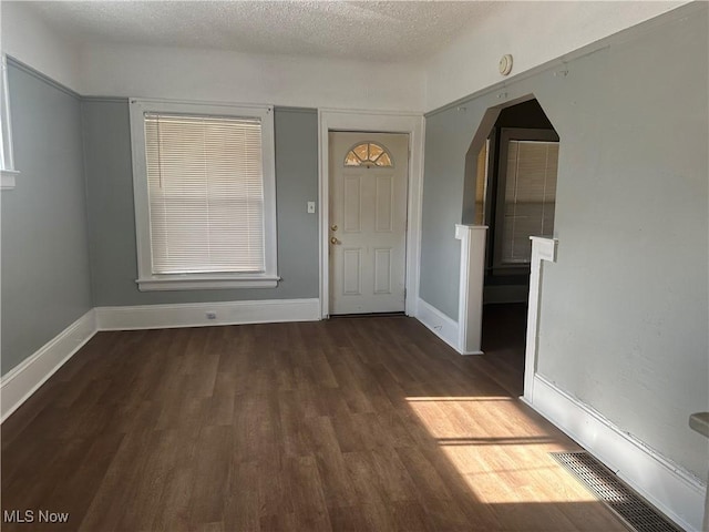 entryway featuring arched walkways, visible vents, a textured ceiling, wood finished floors, and baseboards