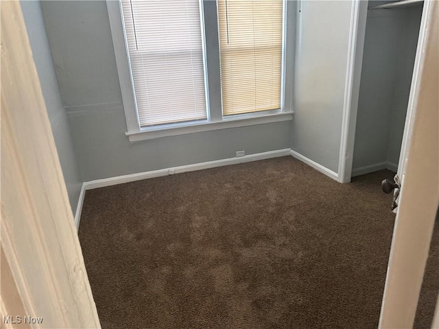 unfurnished bedroom with dark colored carpet, a closet, and baseboards