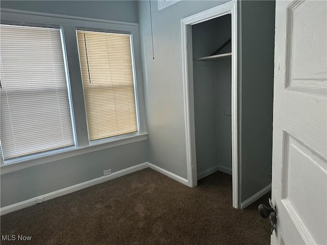 unfurnished bedroom featuring baseboards, dark colored carpet, and a closet