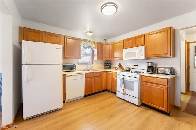 kitchen featuring a toaster, white appliances, a sink, light countertops, and light wood-type flooring