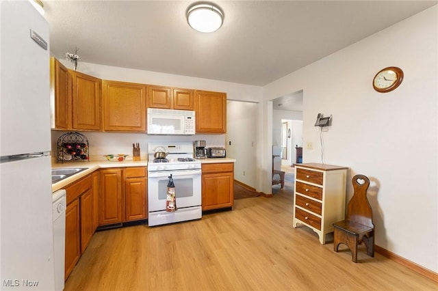 kitchen featuring light countertops, white appliances, brown cabinetry, and light wood-style floors