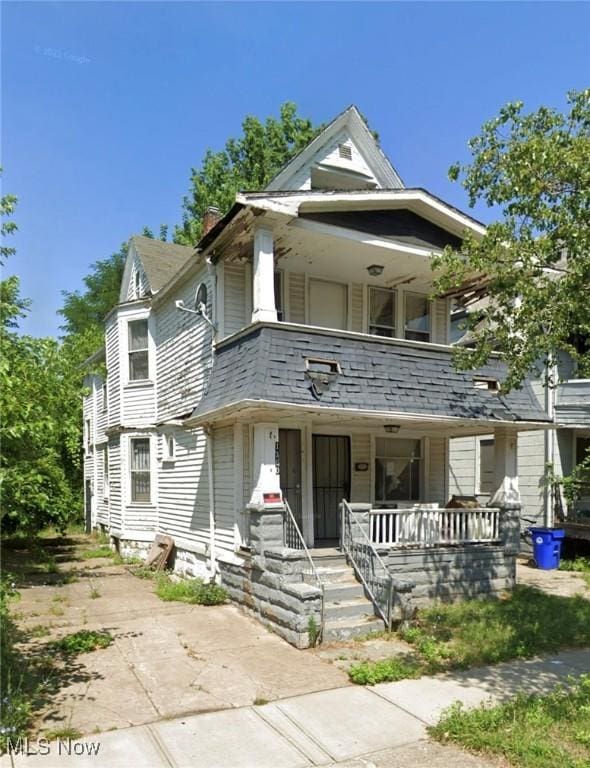 view of front of home with covered porch, roof with shingles, a chimney, and a balcony